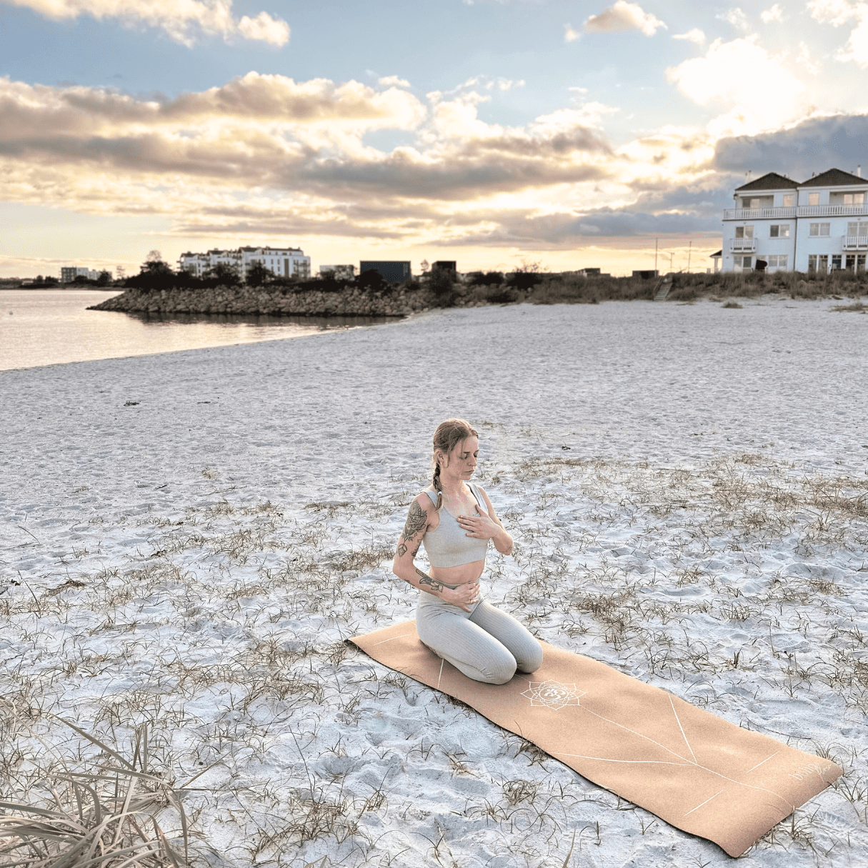 A girl sitting on a cork yoga mat on the beach, practicing breathwork.