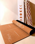 Product shot of the Boho Flow Alignment Cork yoga mat, close up with visible logo, mandala and alignment marks. In the background, the complementary boho bag and packaging box.
