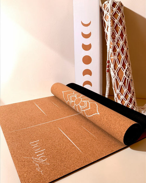 Product shot of the Boho Flow Alignment Cork yoga mat, close up with visible logo, mandala and alignment marks. In the background, the complementary boho bag and packaging box.