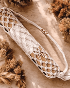 Macrame yoga mat bag containing a cork yoga mat lying on a wooden surface with dried plants