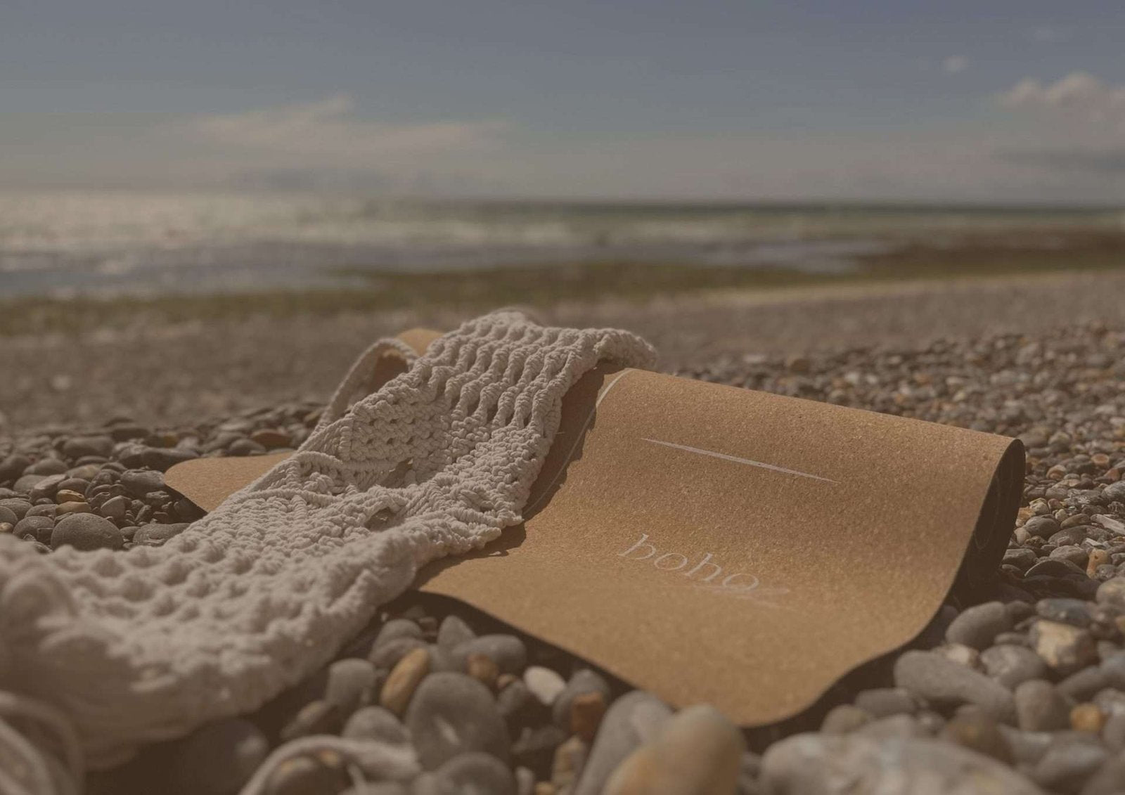 A cork yoga mat with a Macramé carry bag on a pebbly beach