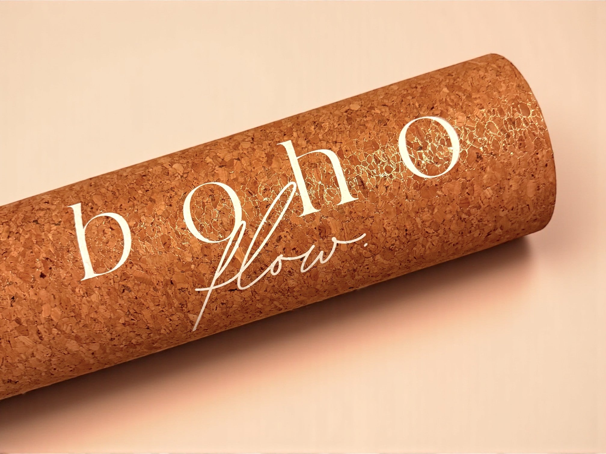 A close up shot of the Boho Flow gold cork yoga mat with the logo 'boho flow' text on a neutral, beige background.