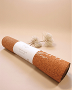 Rolled up cork yoga mat with gold accents on a beige background