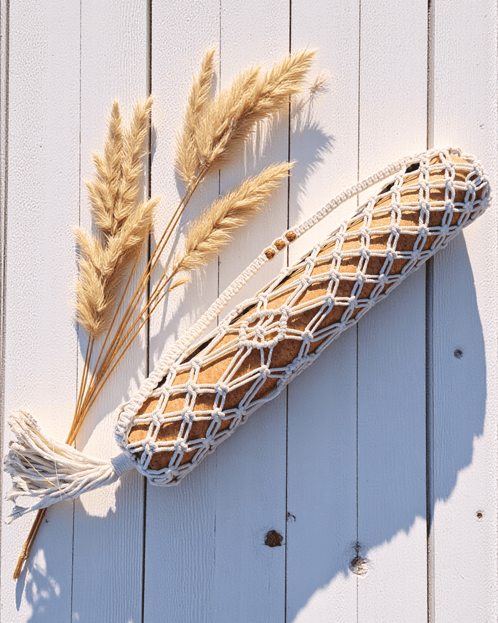 Macrame yoga mat bag hanging with dried pampas grass on a light wooden background