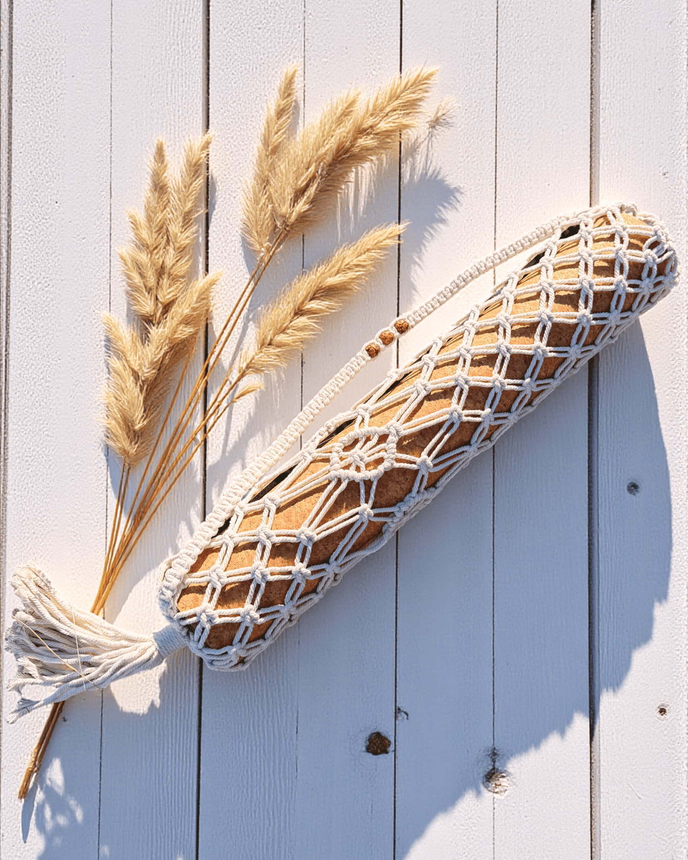 Macrame yoga mat bag hanging with dried pampas grass on a light wooden background