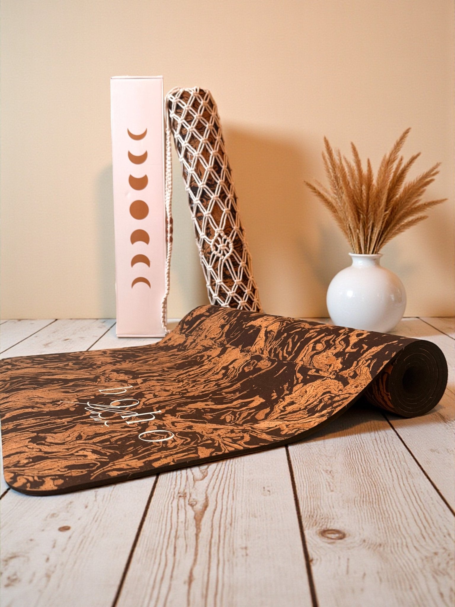 A cork yoga mat partially unrolled on the floor with a macrame yoga mat bag displayed in background.