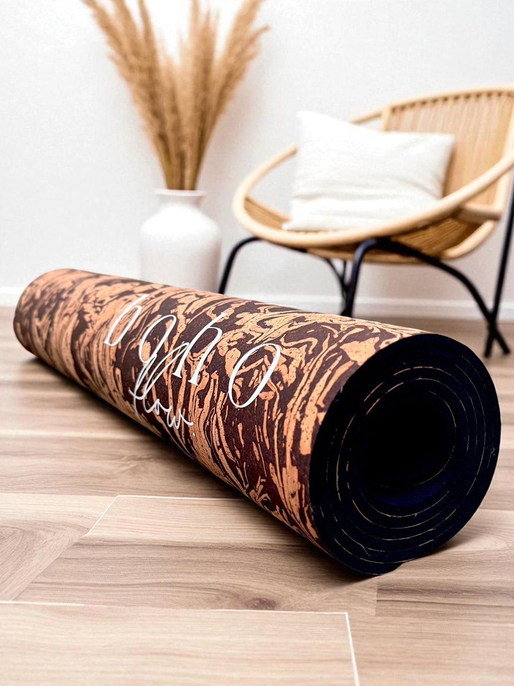 A Coffee infused Cork Yoga Mat rolled up on the floor next to a chair and some dried flowers.