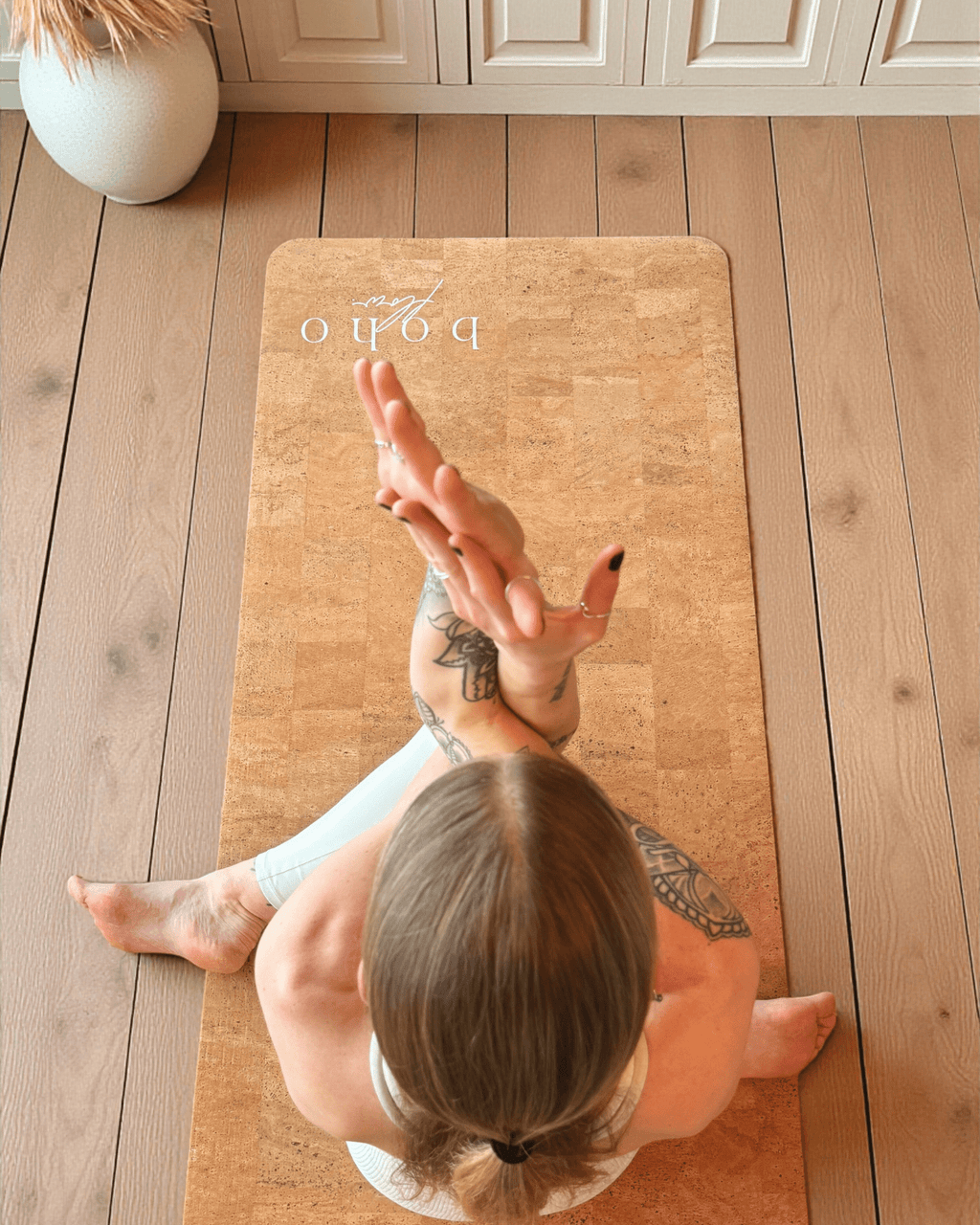 Person practicing yoga on a vegan leather cork mat with 'boho' branding in a home setting.