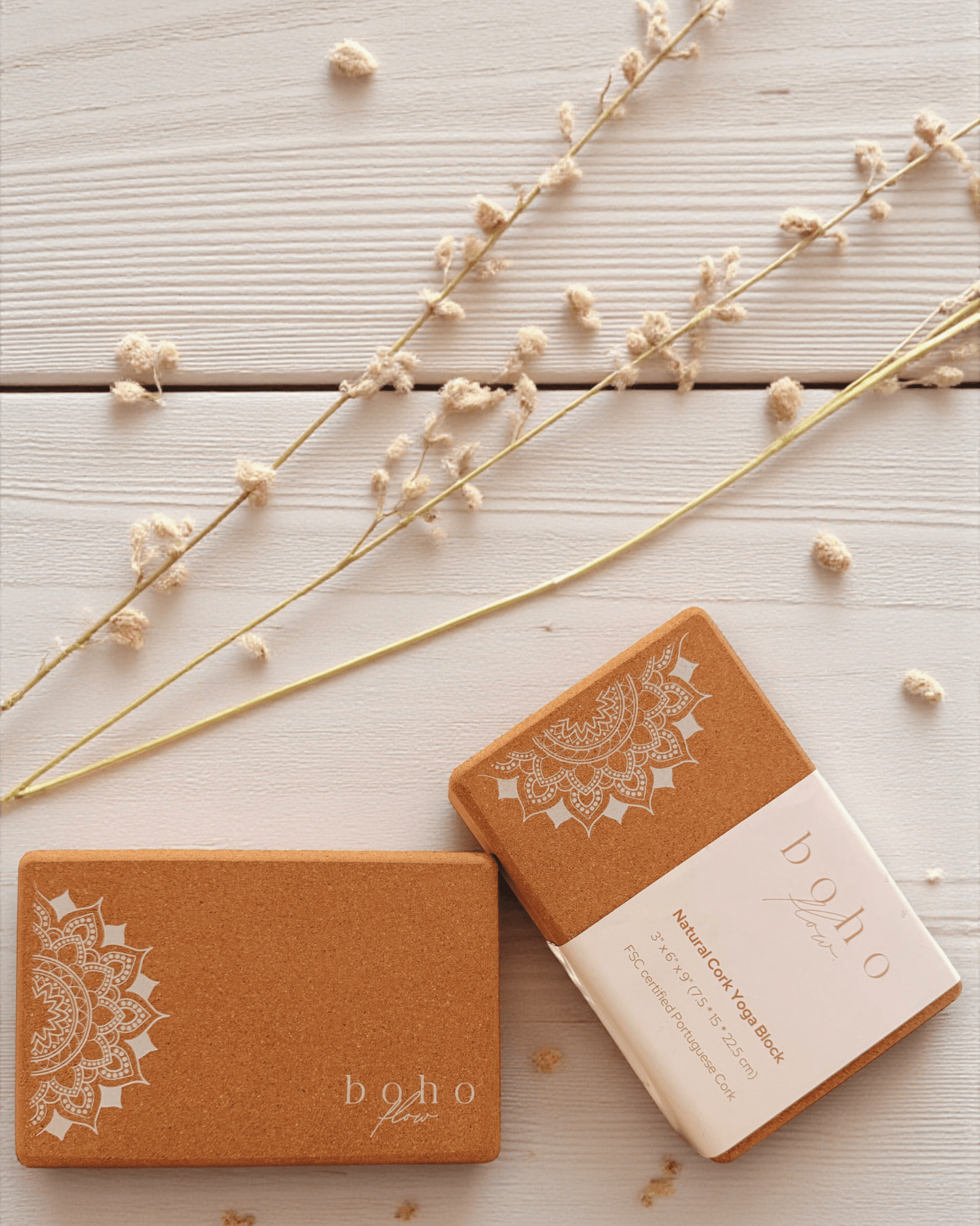 Two cork yoga blocks with white mandala design and 'boho flow' branding on a light wooden surface with dried flowers.