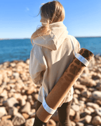 Person carrying a leopard print cork yoga mat on rocky beach with ocean view