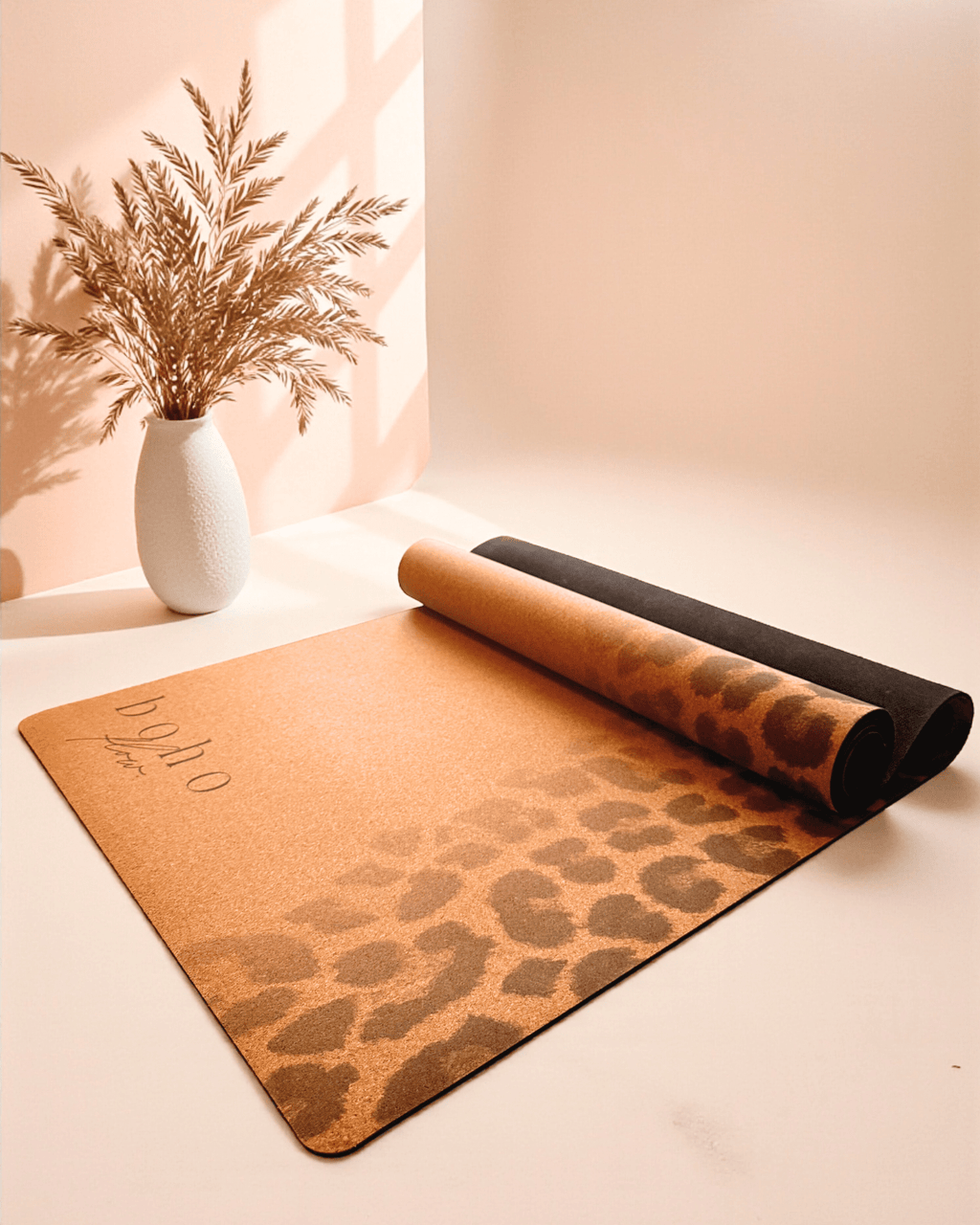 Leopard print cork yoga mat on a light surface with a vase of dried plants in the background.