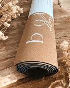 Rolled up cork yoga mat on a wooden surface with dried flowers.