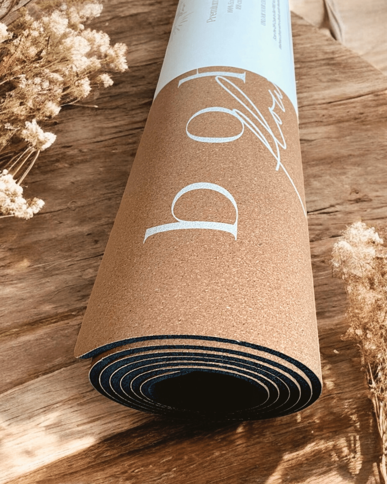 Rolled up cork yoga mat on a wooden surface with dried flowers.