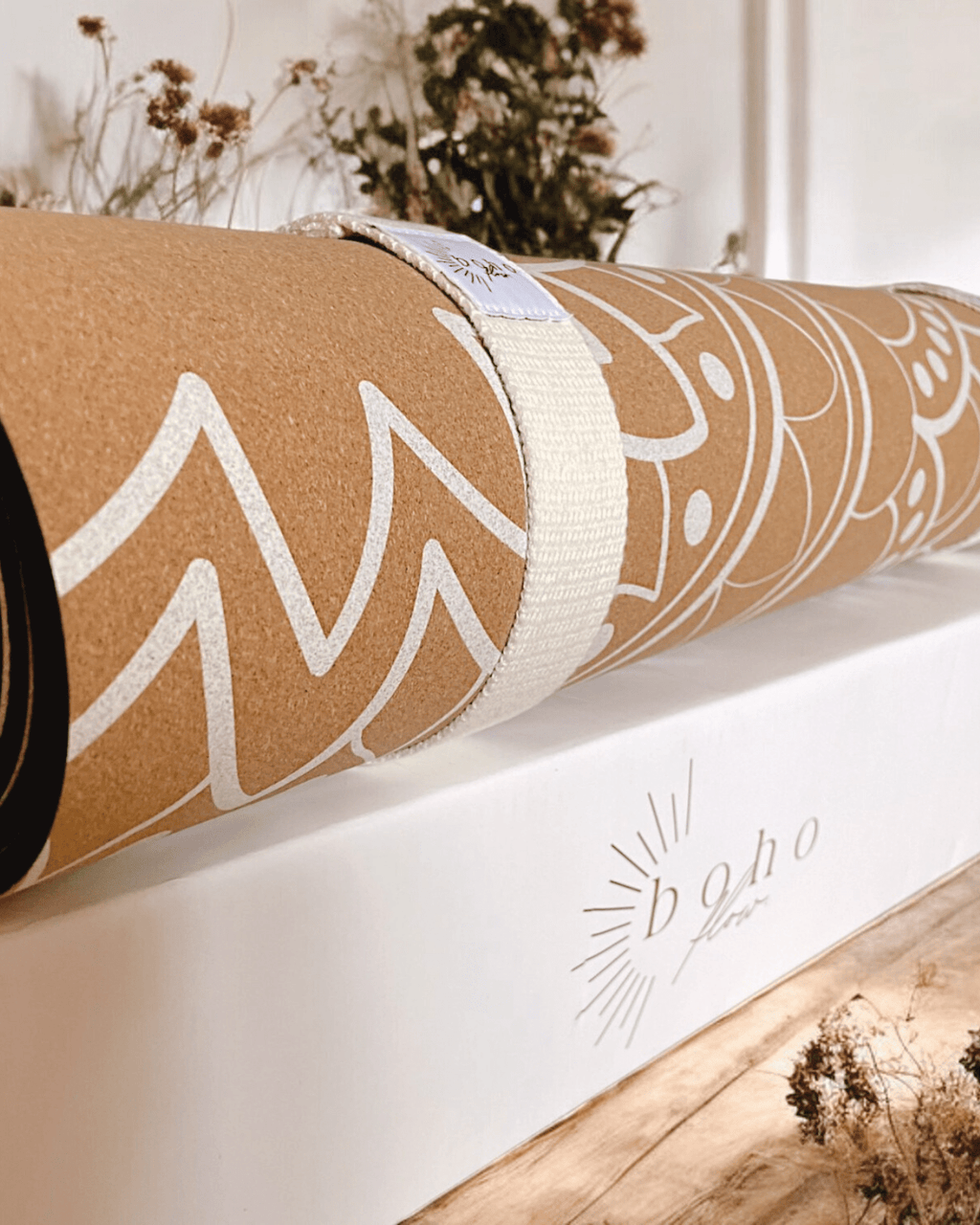 Rolled up cork yoga mat with white mandala on a white box, featuring the brand 'boho flow'.